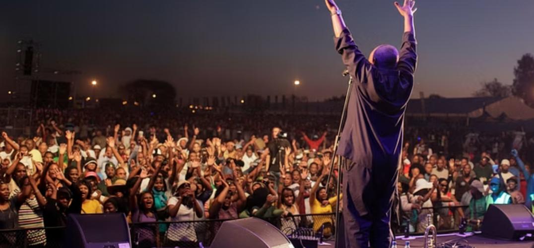 Massive outdoor concert crowd with hands raised in the air, showcasing large-scale music festival production and crowd management expertise